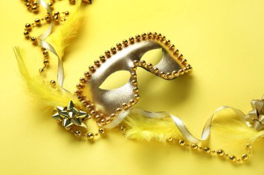Sarı arka planda tüyleri ve boncukları olan güzel altın karnaval maskesi