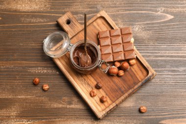 Bir kavanoz çikolata ve ahşap arka planda fındık.