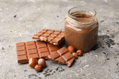 Kavanoz dolusu çikolata serpilmiş ve fındıklar gri arka planda