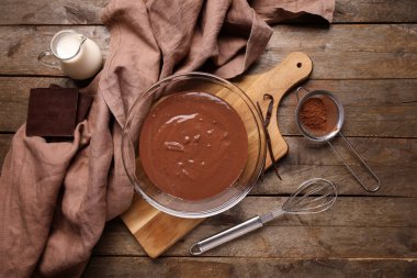 Bir kase sıcak çikolata, bir kavanoz süt ve ahşap fonda elek kakao. Üst görünüm