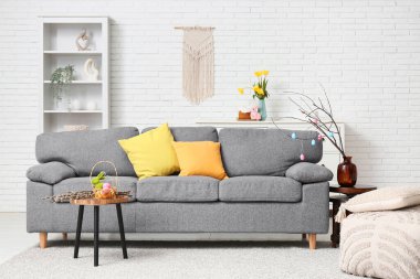 Interior of living room with sofa, Easter rabbit, colorful eggs in basket and pussy willow branches on table