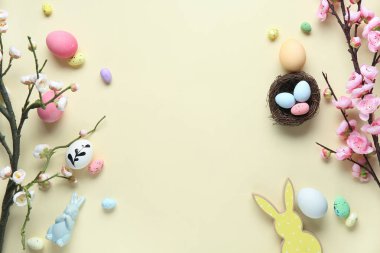Paskalya yumurtalarından, dekordan ve bej arka planda çiçek açan ağaç dallarından yapılmış çerçeve