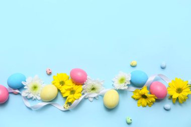 Mavi arka planda Paskalya yumurtası, çiçek ve kurdele kompozisyonu