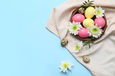 Mavi arka planda Paskalya yumurtası, çiçek ve peçeteyle kase