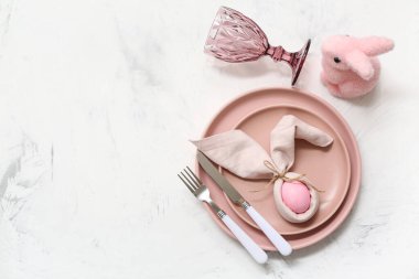 Beyaz arka planda pembe Paskalya yumurtası ve oyuncak tavşanı olan güzel bir masa.
