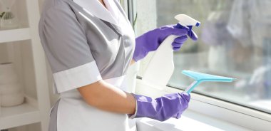 Odanın penceresini temizleyen genç oda hizmetçisi.