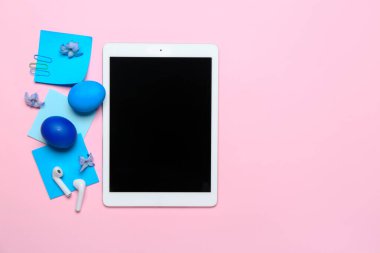Tablet computer with earphones, sticky notes, flowers and Easter eggs on pink background
