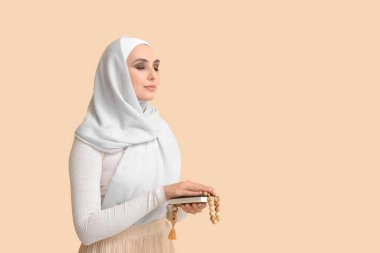 Young Muslim woman with Koran and prayer beads on beige background. Islamic New Year celebration