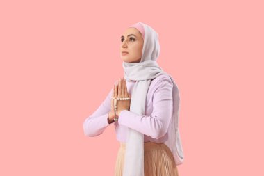 Young Muslim woman with prayer beads on pink background. Islamic New Year celebration
