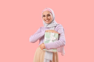 Young Muslim woman with gift on pink background. Islamic New Year celebration
