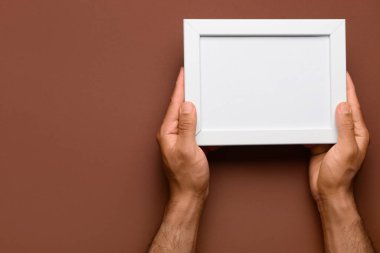 Kahverengi arkaplanda boş fotoğraf çerçevesi tutan adam