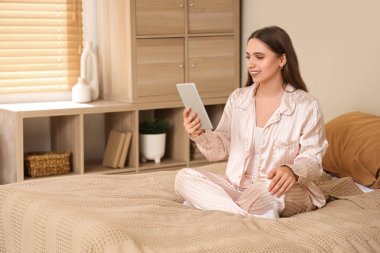 Evde pijamalı, tabletle sohbet eden genç ve güzel bir kadın.