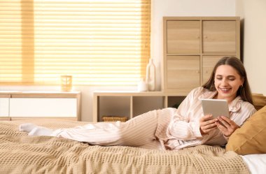 Evde pijamalı, tabletle sohbet eden genç ve güzel bir kadın.