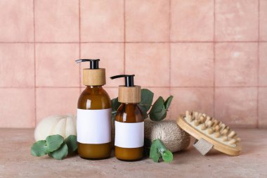 Şampuan şişeleri, banyo süngerleri ve pembe fayans duvarının yanındaki masada yeşil dallarla kompozisyon.