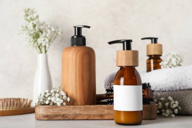 Ahşap tepsiyle kompozisyon, şampuan şişeleri ve çiçekler bej rengi grunge duvarın yanındaki masada, yakın plan.