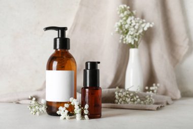 Bej rengi grunge duvarın yanındaki masada şampuan ve çiçek şişeleriyle kompozisyon, yakın plan.