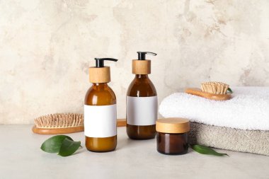 Bej rengi grunge duvarın yanındaki masada şampuan, havlu ve saç fırçası şişeleriyle kompozisyon