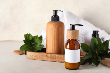 Ahşap tepsiyle kompozisyon, bir şişe şampuan, havlu ve bej rengi grunge duvarın yanındaki masada yeşil dallar, yakın plan.