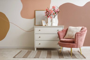 Koltuk, çerçeveli çekmeceler ve odadaki renkli duvarın yanında manolya çiçekleri