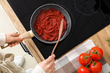 Kızartma tavasında domates ezmesi karıştıran genç bir kadın. Mutfakta kaşıkla.