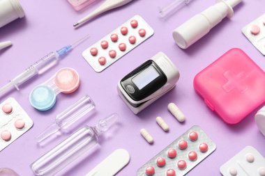 Nabız oksimetresi, steteskop ve eflatun arkaplan üzerindeki ilaçlar, yakın plan.