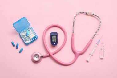 Nabız oksimetresi, steteskop, ilaç kutusu, şırınga ve pembe arka planda ampul bileşimi