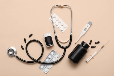 Bej arka planda nabız oksimetresi, steteskop, termometre ve ilaçla bileşim