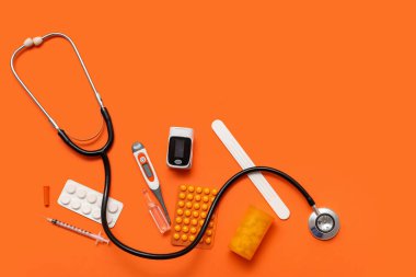 Turuncu arka planda nabız oksimetresi, steteskop ve ilaç bileşimi