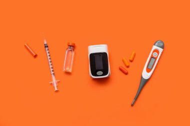 Composition with pulse oximeter, thermometer, pills, syringe and ampule on orange background clipart