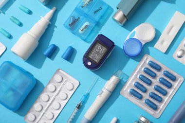 Nabız oksimetresi, konteynır kontak lensler, termometre ve mavi arka planda ilaçlar.