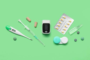 Yeşil zemin üzerinde titreşim oksimetresi, termometresi ve ilaçları olan bileşim