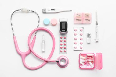 Nabız oksimetresi, steteskop, termometre ve ilaçlar beyaz arkaplanda.