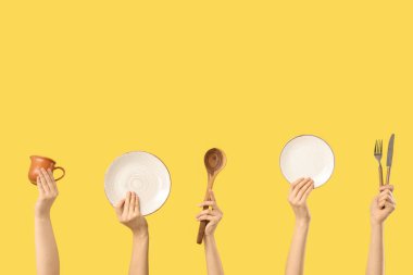 Kadın eli tabaklar, sürahi, çatal, bıçak ve sarı arka planda ahşap kepçe