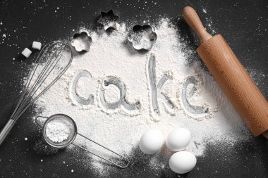 Merdaneden yapılmış çerçeve, hamur malzemeleri ve siyah arkaplanda un üzerine kelime keki.