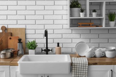 Ahşap mutfak tezgahı, temiz tabaklar ve seramik lavabo, hafif tuğla duvarın yanında.