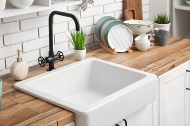 Mutfak tezgahında lavabo, temiz tabaklar ve hafif tuğla duvarın yanında bitkiler var.