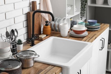 Seramik lavabo ve temiz tabaklar hafif tuğla duvarın yanındaki ahşap tezgahta.