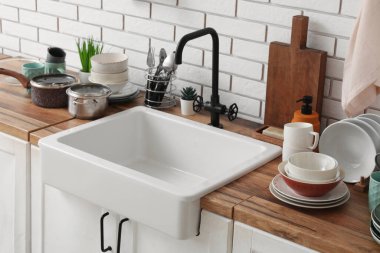 Seramik lavabo ve temiz tabaklar hafif tuğla duvarın yanındaki ahşap tezgahta.