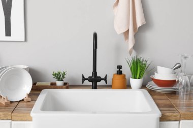 Seramik lavabo, temiz tabak ve bitkiler gri duvarın yanındaki ahşap mutfak tezgahında.