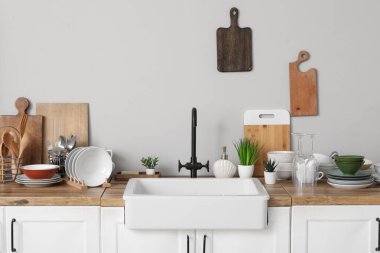 Ahşap tezgah, şık seramik lavabo, temiz tabaklar ve gri duvarın yanında mutfak aletleri.