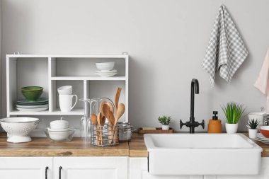 Seramik lavabo, temiz bulaşıklar ve ahşap mutfak tezgahındaki raf ünitesi.
