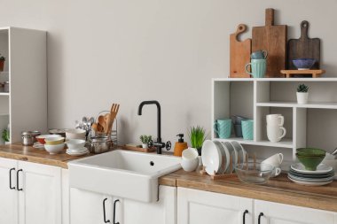 Şık seramik lavabo, temiz bulaşıklar ve ahşap mutfak tezgahındaki raf ünitesi.