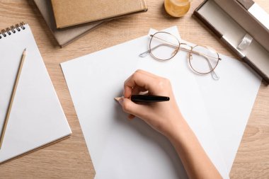 Dolma kalemli kadın eli, boş kağıt çarşaflar, gözlük, kırtasiye ve ahşap zemin üzerine kitaplar, yakın plan.