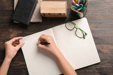 Kadın deftere, gözlüğe, kırtasiyeye ve küp takvimine bir şeyler yazıyor.