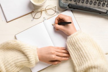 Deftere bir şey yazan kadın, gözlük ve daktilo açık tahta arka planda, yakın plan.