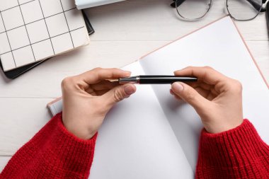 Dolma kalemli kadın eller, defterler ve gözlük açık ahşap masada, yakın plan.