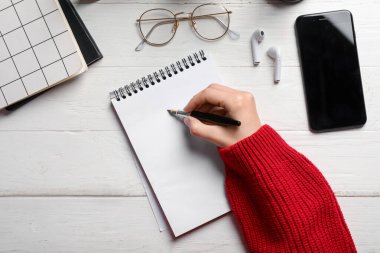 Deftere, gözlüğe, kulaklığa ve cep telefonuna beyaz ahşap masaya bir şeyler yazan kadın.