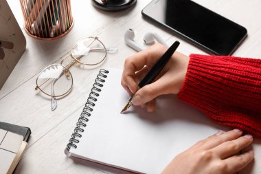 Deftere, gözlüğe, kulaklığa ve cep telefonuna beyaz ahşap masaya bir şeyler yazan kadın.