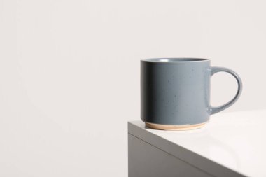 Beyaz duvarın yanındaki masada seramik gri kupa.