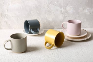 Beyaz duvarın yanındaki masada seramik bardaklar ve tabaklarla kompozisyon